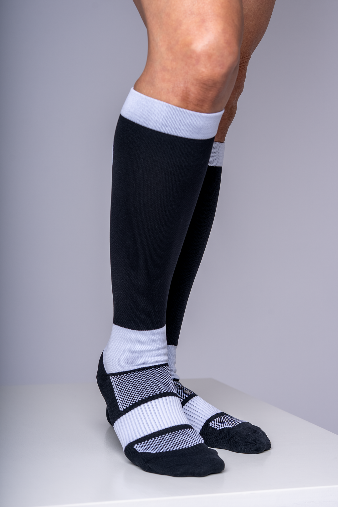 Person wearing black knee-high socks with white accents on a plain background