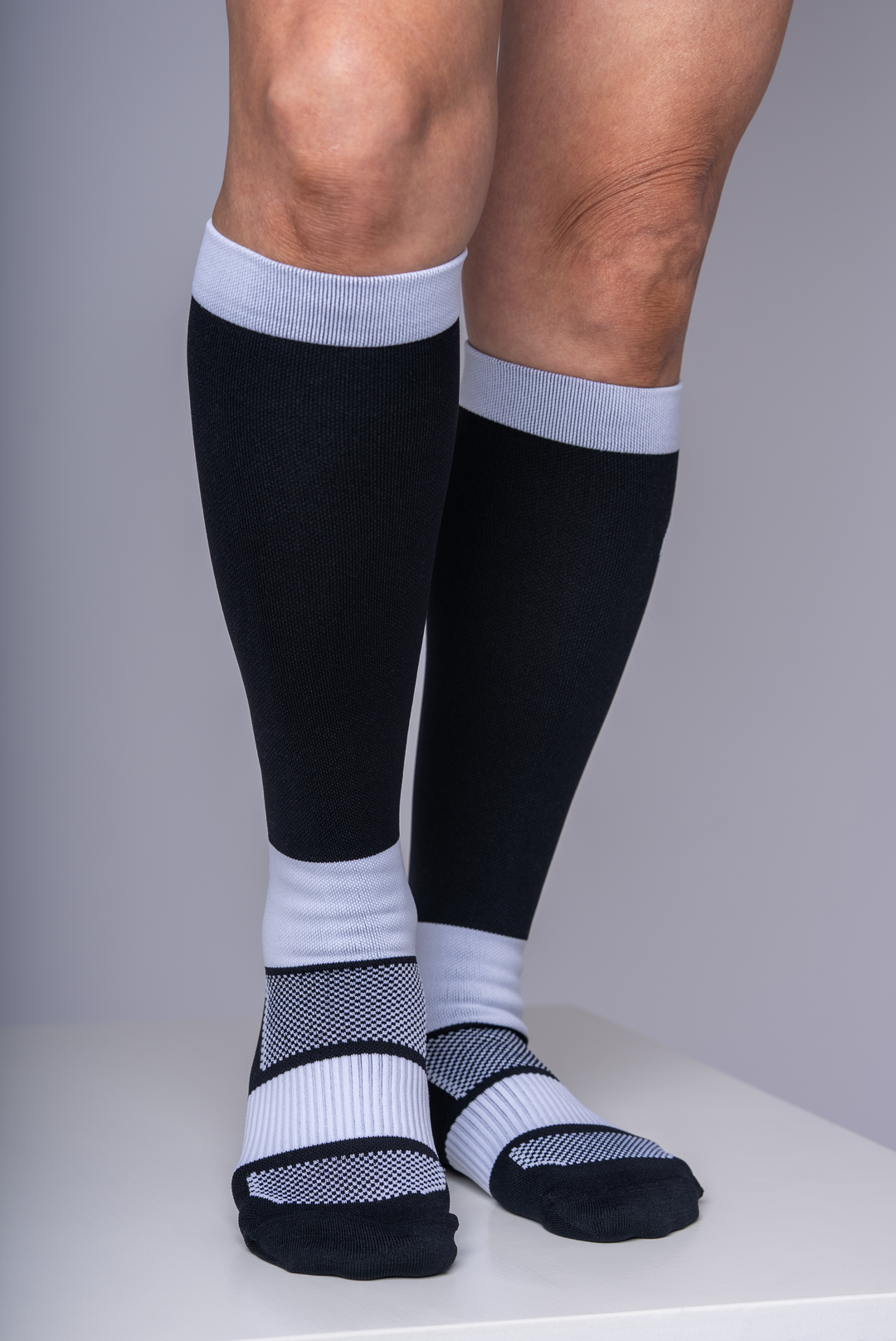 Person wearing black knee-high socks with white accents on a gray background