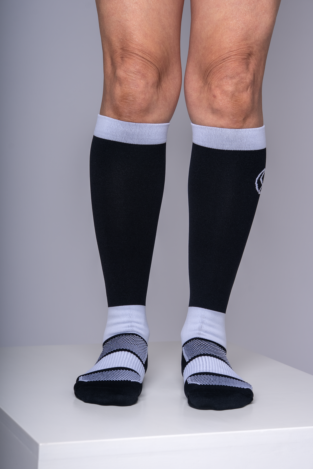 Person wearing black knee-high compression socks with white accents on a plain background